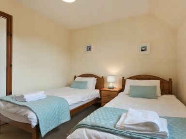 A bedroom with two single beds with blue quilts and pillows and a wooden nightstand with a lamp at Smithy Court in Craster
