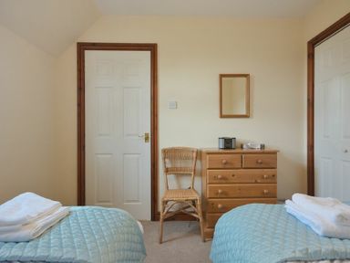A bedroom with two beds with blue covers a wooden chair a wooden chest of drawers and a mirror on the wall at Smithy Court in Craster