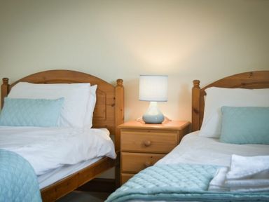 A bedroom with two wooden beds a bedside table and a lamp at Smithy Court in Craster