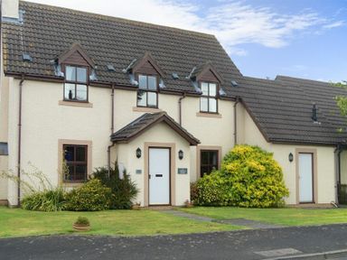 A cream color two story house with brown roof tiles and green bushes in front at Smithy Court in Craster
