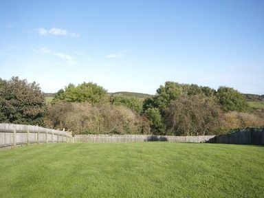 A fenced grassy backyard with trees and shrubs in the background at Smithy Court in Craster