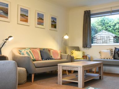 A living room with a sofa, armchairs, cushions, a coffee table, two lamps, framed pictures on the wall, and a window showing a garden shed at Barmoor in Embleton