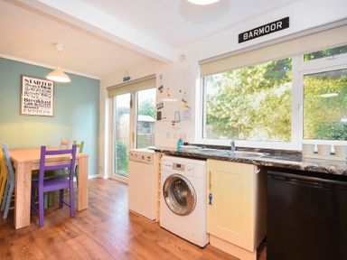A kitchen dining area with a wooden table and colorful chairs near a glass door and a kitchen counter with appliances at Barmoor Embleton