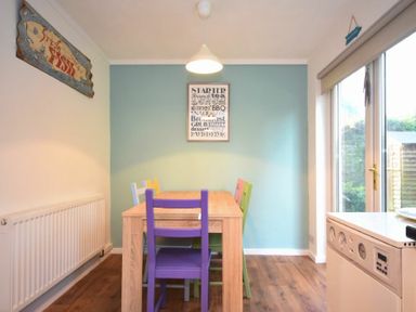 A dining area with a wooden table and colorful chairs by a light blue wall and sliding glass door at Barmoor in Embleton