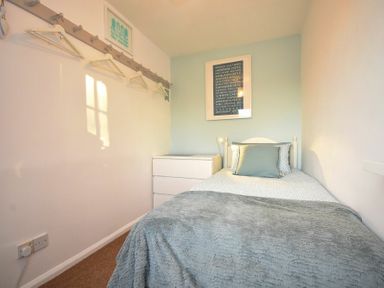 A bedroom with a single bed a grey blanket a bedside table with a lamp and framed pictures on the wall at Barmoor in Embleton