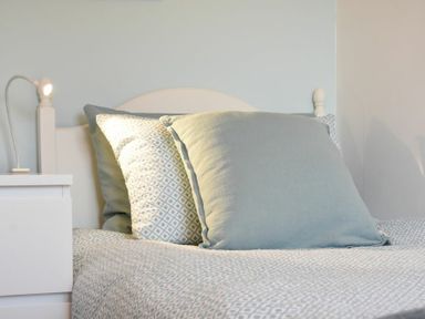 A bed with patterned and plain pillows and a bedside table with a lamp at Barmoor in Embleton