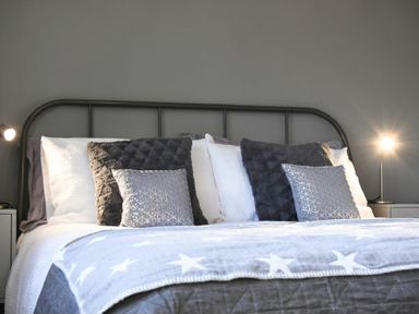 A bed with multiple pillows and a star patterned blanket with two bedside lamps at Barmoor in Embleton