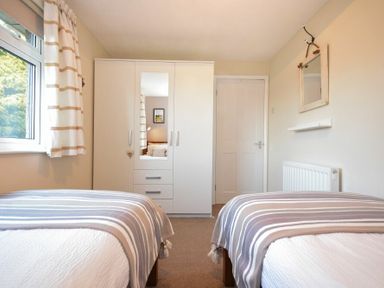 A bedroom with two single beds a wardrobe with mirror a window with striped curtains and a wall mirror at Barmoor in Embleton