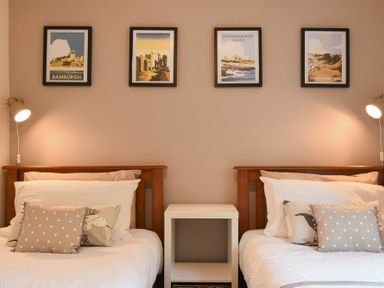A bedroom with two single beds separated by a white nightstand and wall art above the beds at Barmoor in Embleton