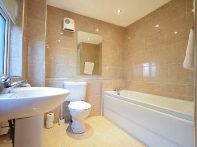 A bathroom with a sink, toilet, and bathtub with tiled walls and floor at Barmoor in Embleton