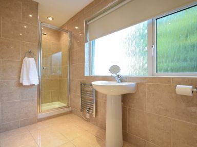 A bathroom with a glass shower cubicle a pedestal sink and a window at Barmoor in Embleton