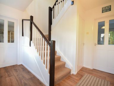 A stairway with brown carpeting and white railings in a hallway with wood flooring and white doors at Barmoor in Embleton