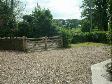 A gravel driveway with a wooden gate and green hedges at Barmoor in Embleton
