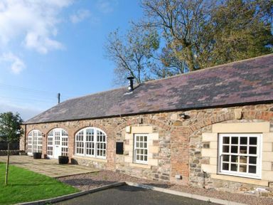 A stone cottage with white framed windows and a tiled roof at Lapwing Cottage in Bamburgh