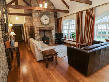 A living room with two sofas a stone fireplace and large windows with curtains at Lapwing Cottage in Bamburgh