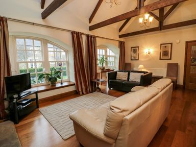 A living room with two sofas a television large windows and exposed ceiling beams at Lapwing Cottage in Bamburgh