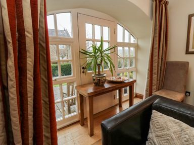 A wooden table with a potted plant and a tray of shells in front of a windowed door with striped curtains and a chair nearby at Lapwing Cottage in Bamburgh