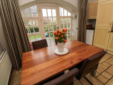 A dining table with a vase of orange tulips near glass doors and striped curtains at Lapwing Cottage in Bamburgh