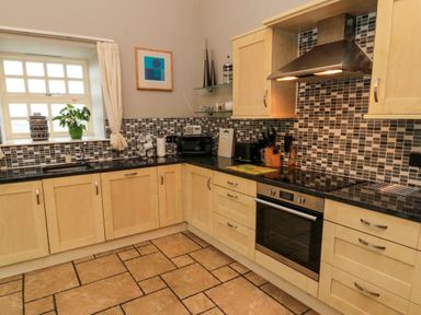 A kitchen with wooden cabinets and black countertops with a window above the sink at Lapwing Cottage in Bamburgh