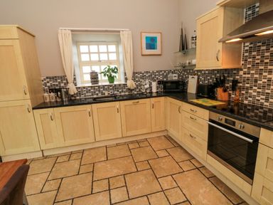 A kitchen with light wood cabinets black countertops a tiled backsplash and a patterned tile floor at Lapwing Cottage in Bamburgh