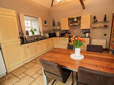 A kitchen with wooden cabinets a wooden dining table with four chairs and a vase of orange flowers at Lapwing Cottage Bamburgh