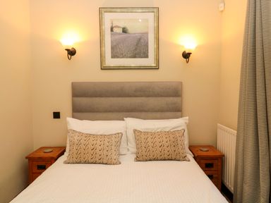 A bedroom with a bed with two patterned pillows two wooden bedside tables and a framed picture above the bed at Lapwing Cottage in Bamburgh