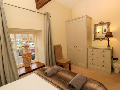 A bedroom with a bed with rolled towels a window with curtains a wardrobe a chair a dresser with a lamp and mirror at Lapwing Cottage in Bamburgh