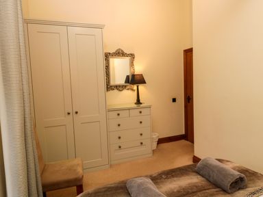 A bedroom with a wardrobe chest of drawers chair and bed with towels at Lapwing Cottage in Bamburgh