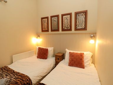 A bedroom with two single beds a small wooden nightstand between them and four framed pictures above the beds at Lapwing Cottage in Bamburgh
