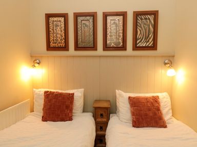A bedroom with two single beds a wooden bedside table wall lights and four framed animal print pictures at Lapwing Cottage Bamburgh