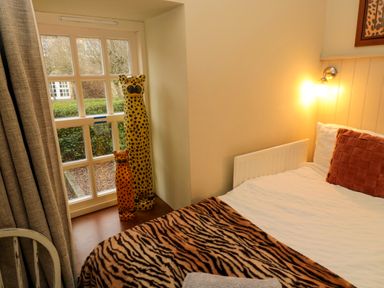 A bedroom with a bed covered in a tiger print blanket and two cheetah sculptures by a window at Lapwing Cottage in Bamburgh