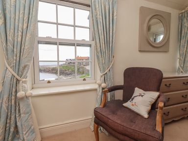 A sitting room with a window and a chair at Marie's Cottage, Craster