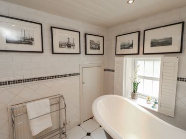 A bathroom featuring a bathtub, photographs on the wall and a window at Marie's Cottage in Craster