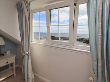 A bedroom with a window overlooking the ocean at Marie's Cottage in Craster