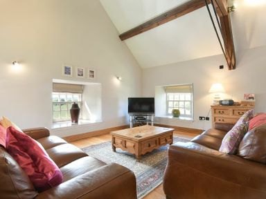 A living room with two leather sofas a wooden coffee table a TV and wooden beams at Budle Sands in Bamburgh