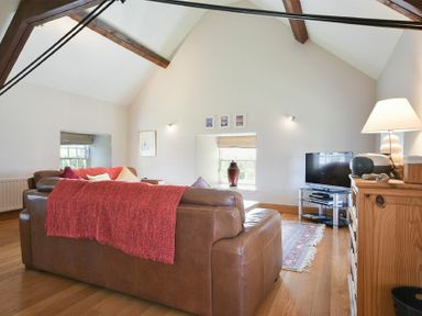 A living room with brown leather sofas and a red throw blanket a wooden cabinet with a lamp a television on a stand and wooden ceiling beams at Budle Sands Bamburgh