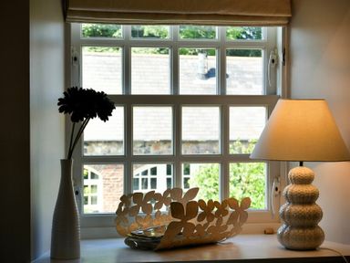 A window with a white vase with flowers a decorative bowl and a lamp on the sill at Budle Sands in Bamburgh