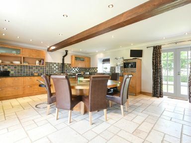 A kitchen with a round wooden table surrounded by six brown chairs wooden cabinets with tiled backsplash and French doors with curtains at Budle Sands in Bamburgh