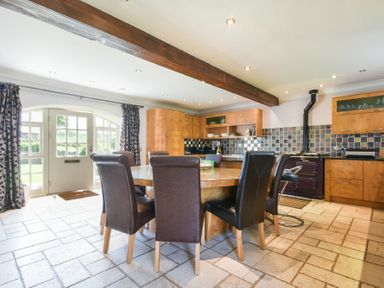 A kitchen with a wooden dining table and leather chairs near a tiled backsplash and a door with curtains at Budle Sands in Bamburgh