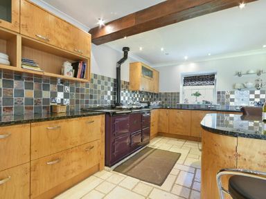 A kitchen with wooden cabinets a black stove tiled backsplash and a countertop with a bar stool at Budle Sands in Bamburgh