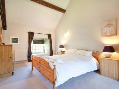 A bedroom with a wooden bed a window with curtains and bedside tables with lamps at Budle Sands in Bamburgh