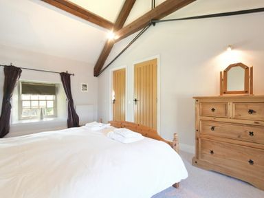 A bedroom with a wooden bed and dresser with mirror near two wooden doors at Budle Sands in Bamburgh