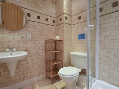 A bathroom with a white toilet a glass shower cubicle a wall-mounted sink a round mirror and a wooden shelving unit at Budle Sands in Bamburgh