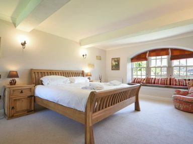 A bedroom with wooden bed and side tables a window seat with cushions and an armchair at Budle Sands in Bamburgh