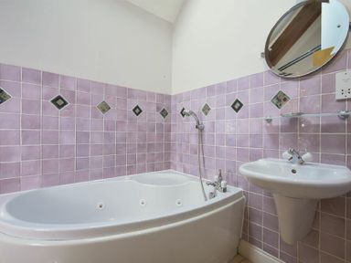 A bathroom with a bathtub a shower mirror and a sink with purple tiled walls at Budle Sands in Bamburgh