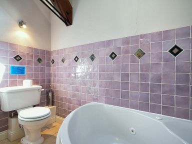 A bathroom with a toilet, a bathtub, purple tiled walls, and a wooden ceiling beam at Budle Sands in Bamburgh