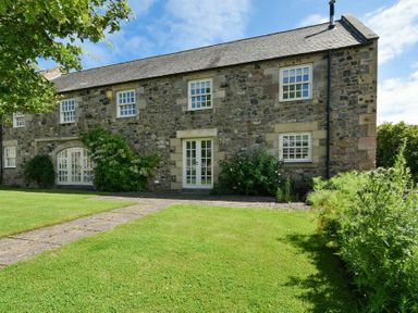 An exterior view of a stone house with grass lawn and bushes at Budle Sands in Bamburgh