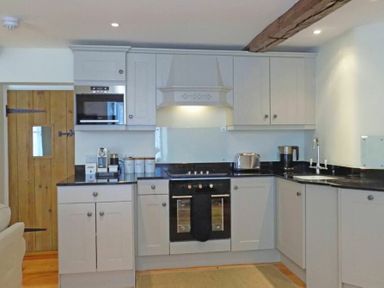 A kitchen with white cabinets black countertops a stove toaster and wooden door at Dorothy Forster Court in Alnwick