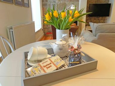 A dining table with a tray containing a teapot cups shortbread fingers and a wrapped gift with yellow flowers in a vase in the background at Dorothy Forster Court in Alnwick