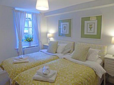 A bedroom with two single beds yellow patterned bedding pillows and towels beside a window at Dorothy Forster Court in Alnwick